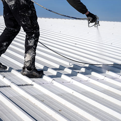 a person in black scrubs spraying solar reflective paint onto an aluminium roof