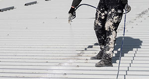 a person standing on an aluminium roof spraying a solar control paint